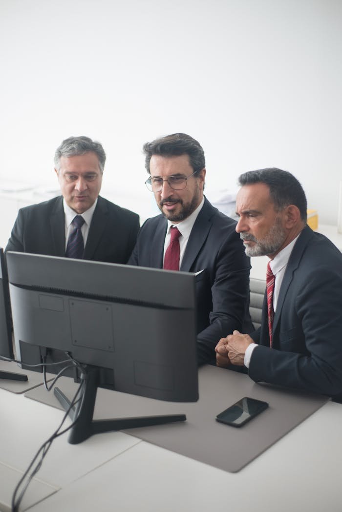 Three businessmen in corporate attire working together at a desk in an office environment.