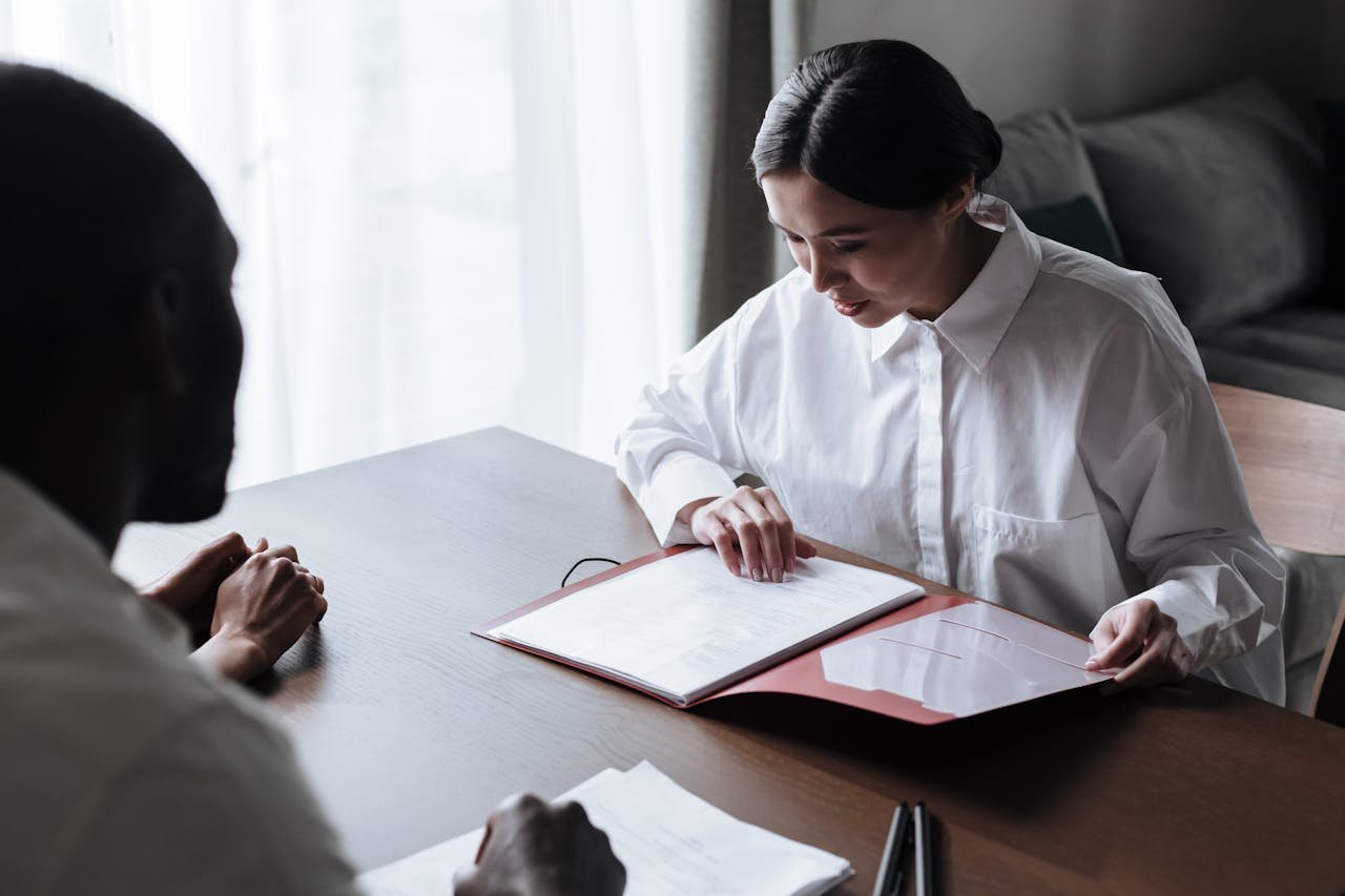 Professional businesswoman discussing documents with colleague at a desk indoors.